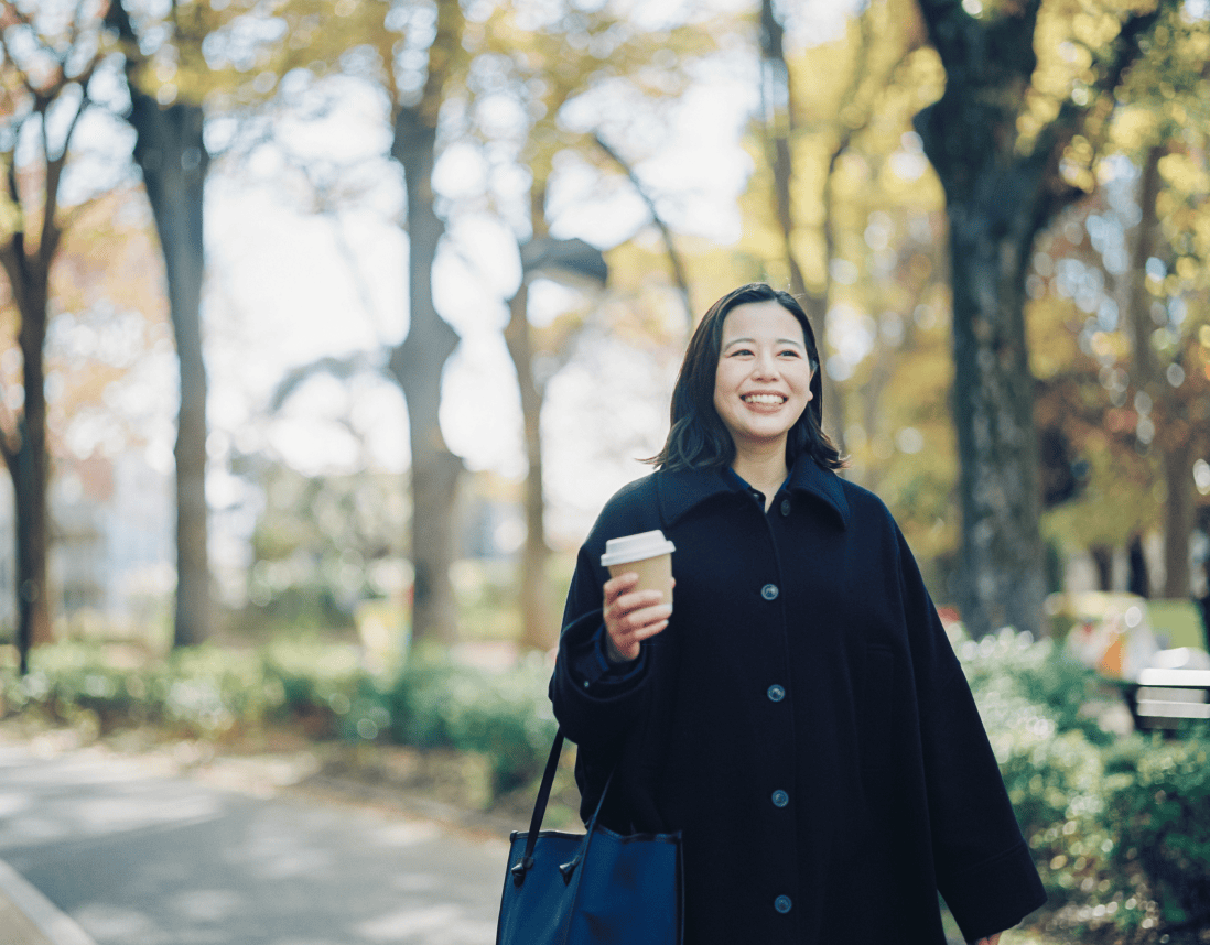 コーヒー片手に笑顔で散歩している女性。