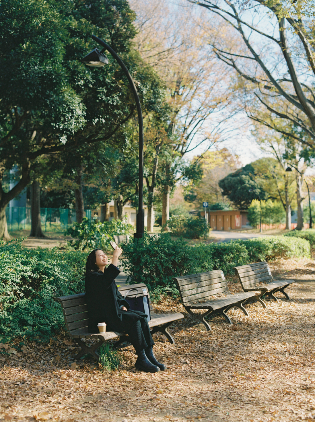 公園のベンチでスマートフォンを利用して風景を撮影している女性。