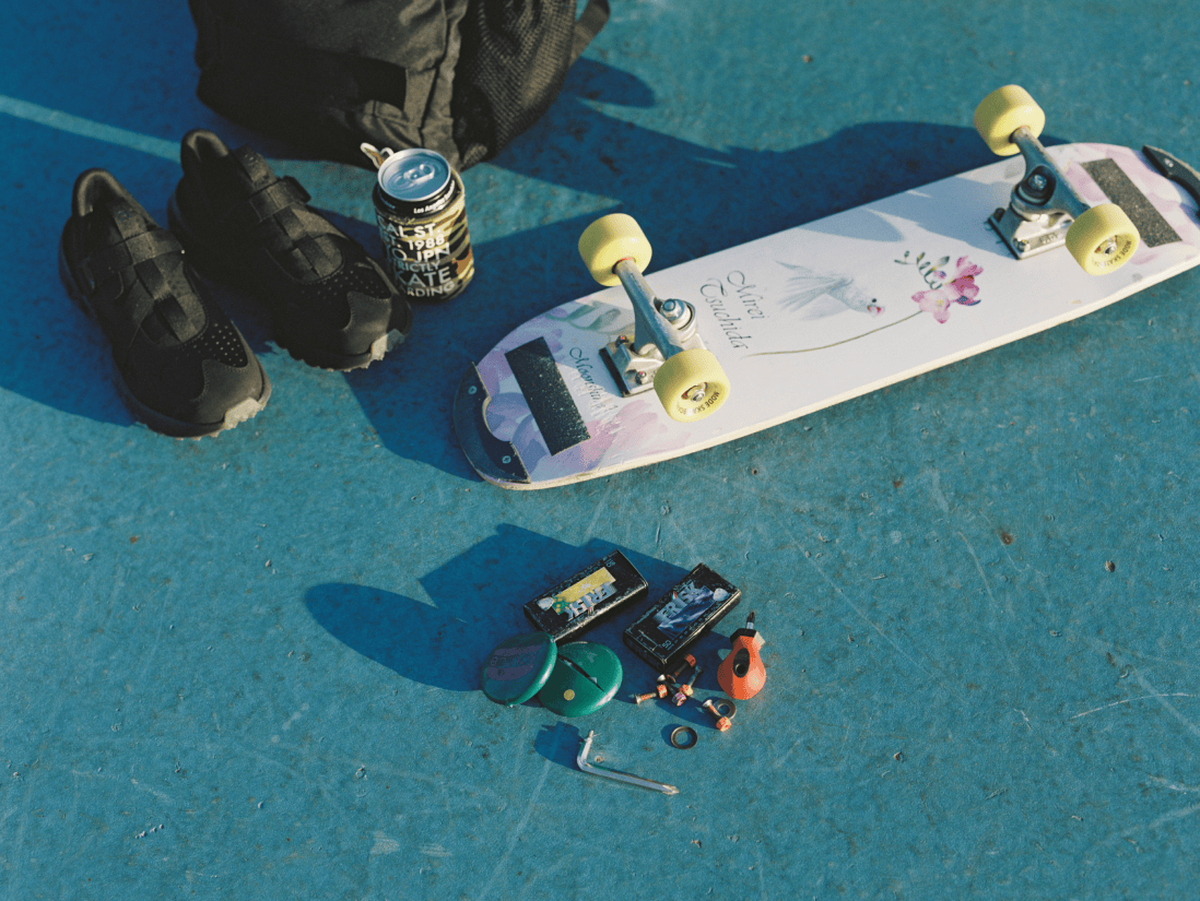 スケートボード、靴、ドリンク、フリスク、工具などが地面に置かれている。