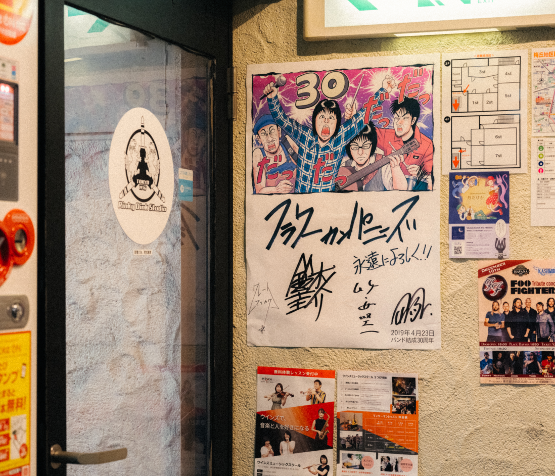 フラワーカンパニーズのサインが入ったポスターと様々なアーティストのチラシが貼られた壁。