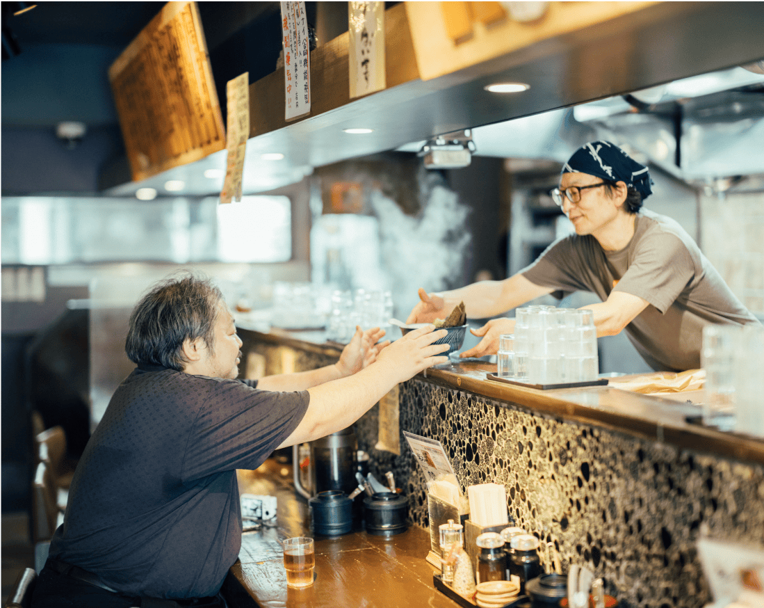 店長さんからラーメンを受け取る男性。