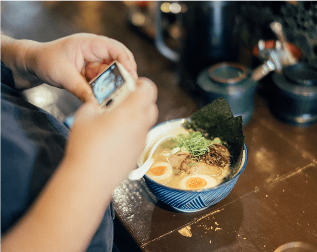 器に盛り付けられたラーメンとそれを撮影する男性の手。