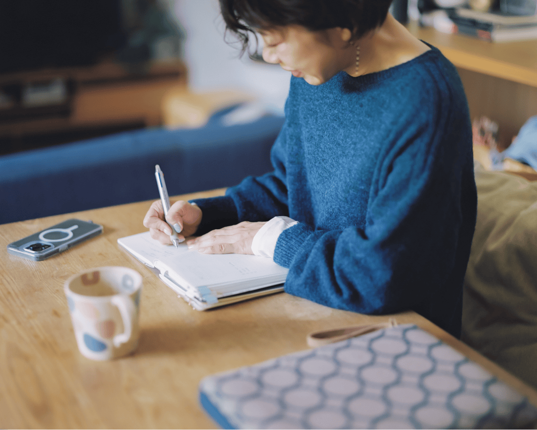 手帳に何かを書いている青い服を着た女性。